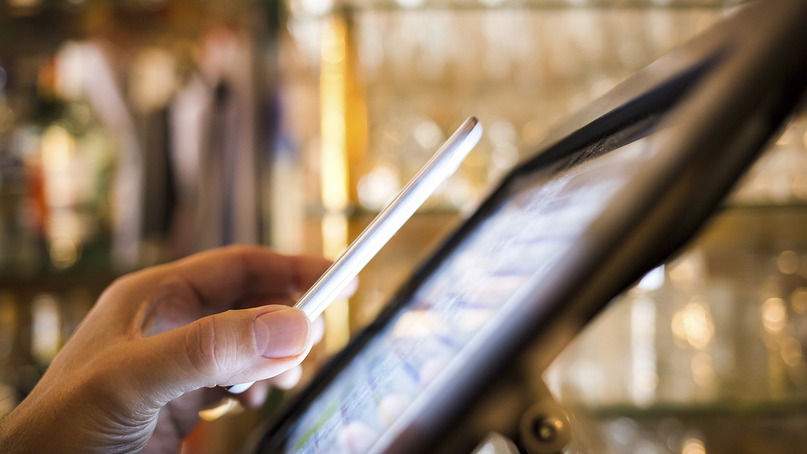 A hand holding a mobile phone over a POS completing a contactless transaction.