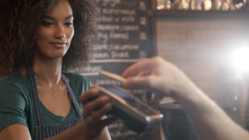 A barista accepting a customer payment via a smart phone at a POS device.
